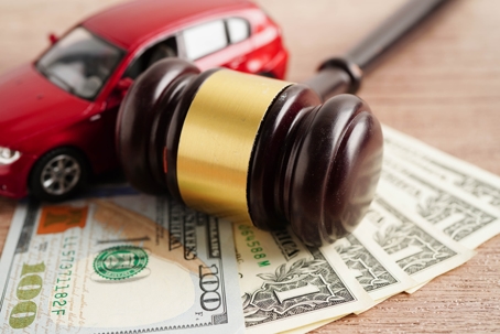 Gavel resting on US dollar bills beside a red toy car, symbolizing car accident legal fees or settlement costs.